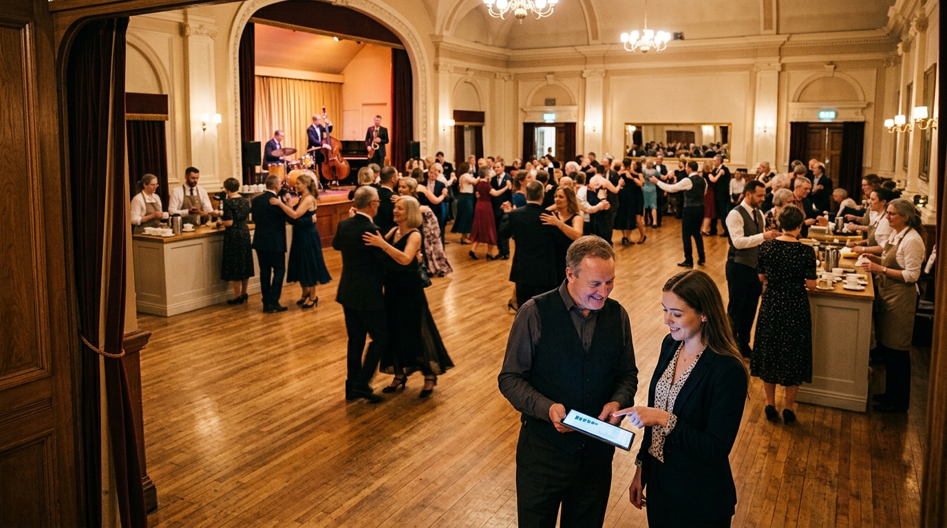 Dance hall owner and a marketing consultant review a tablet as couples waltz across a sprung floor